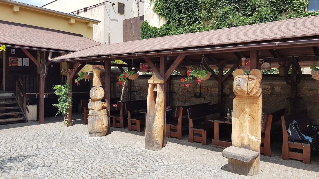 Kryté venkovní posezení s dřevěnými stoly a vyřezávanými dřevěnými sochami
